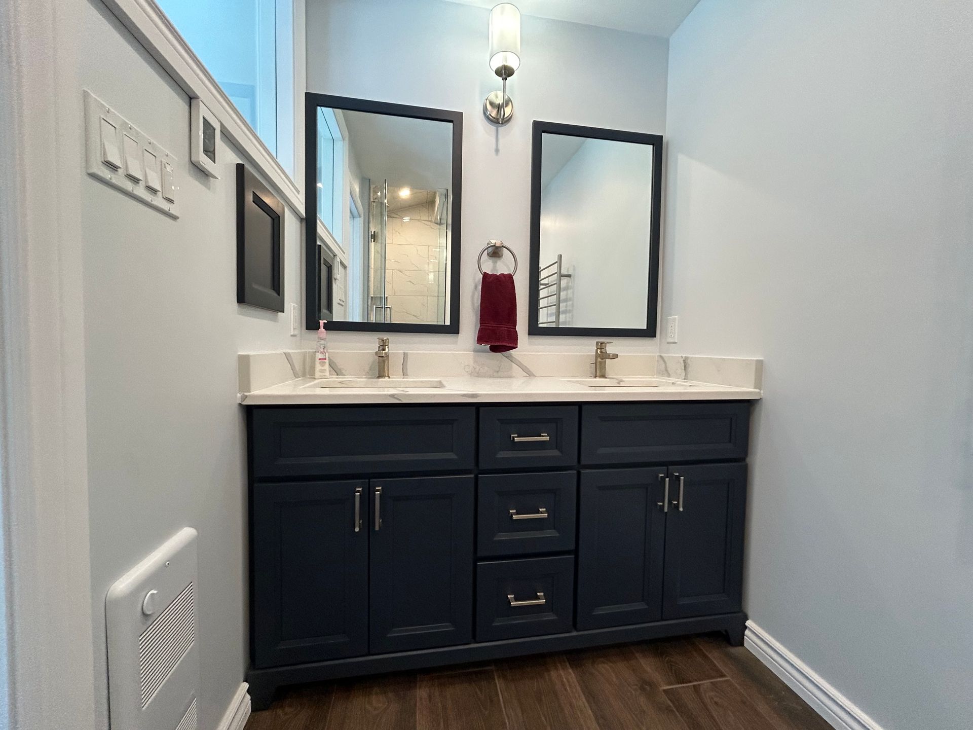 Dark blue double vanity in bathroom with two mirrors, silver fixtures, and light blue walls.
