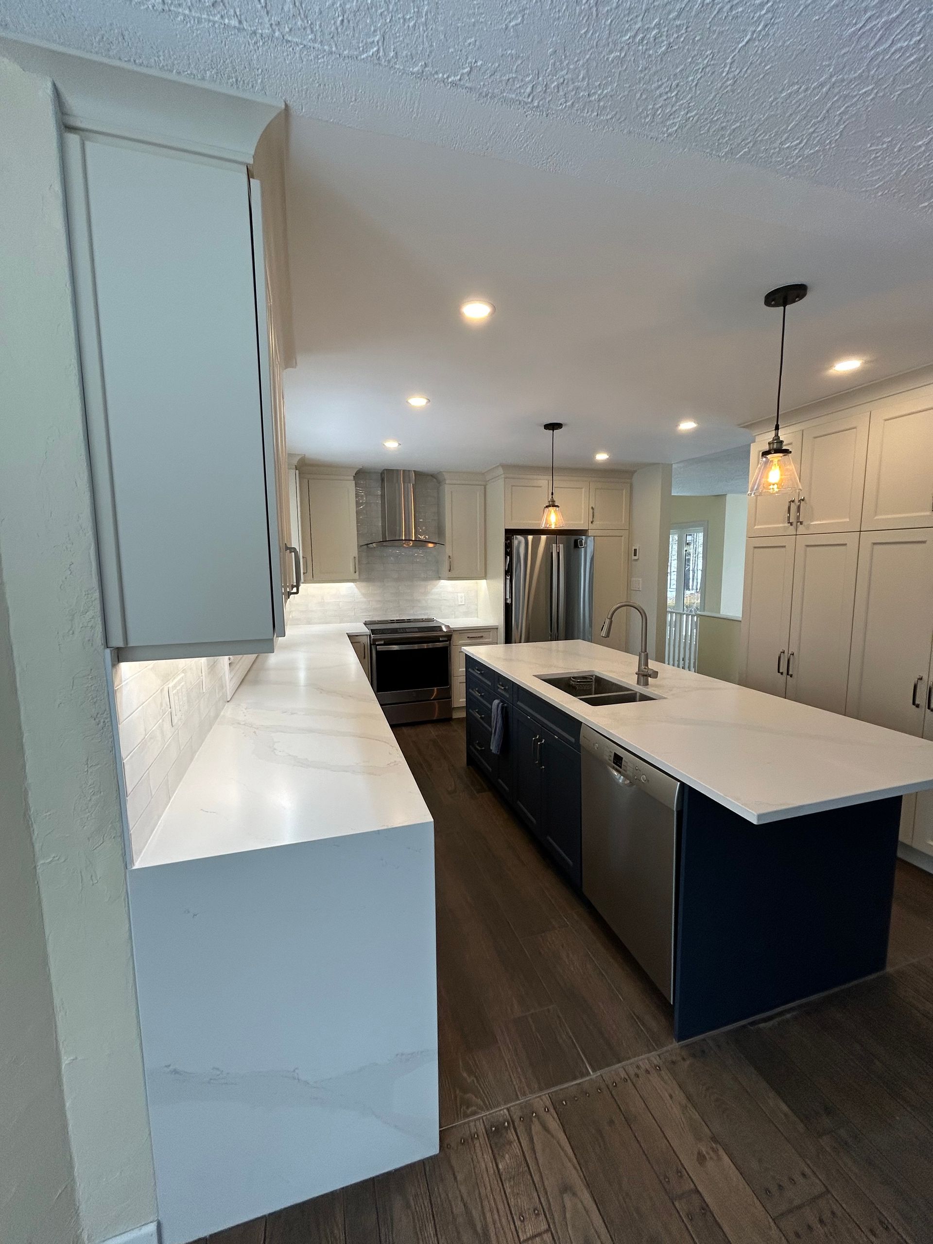 Modern kitchen with white countertops and cabinets, a dark blue island, and stainless steel appliances.