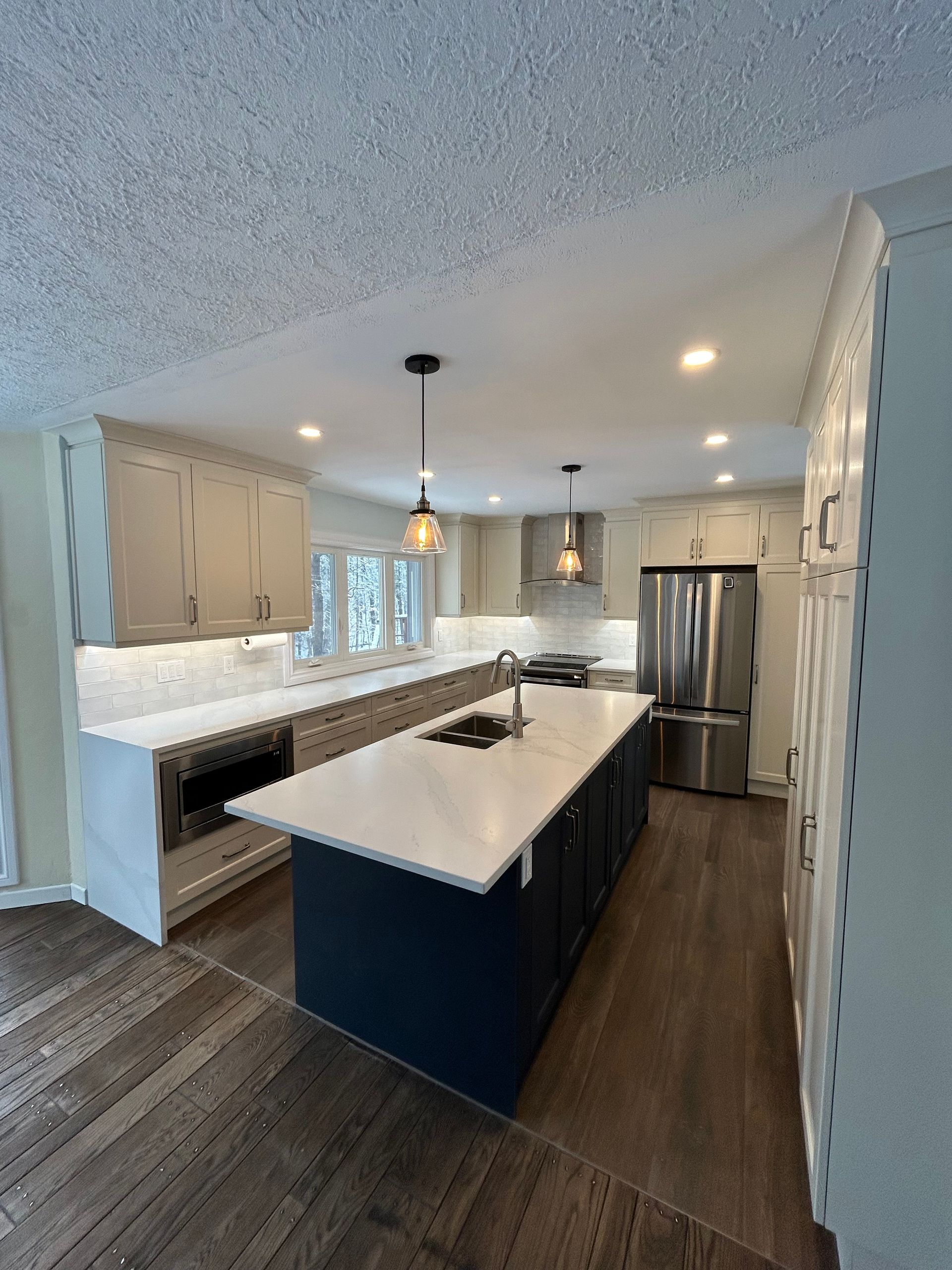 Modern kitchen remodel with white cabinets, blue island, stainless appliances, and wood floors.