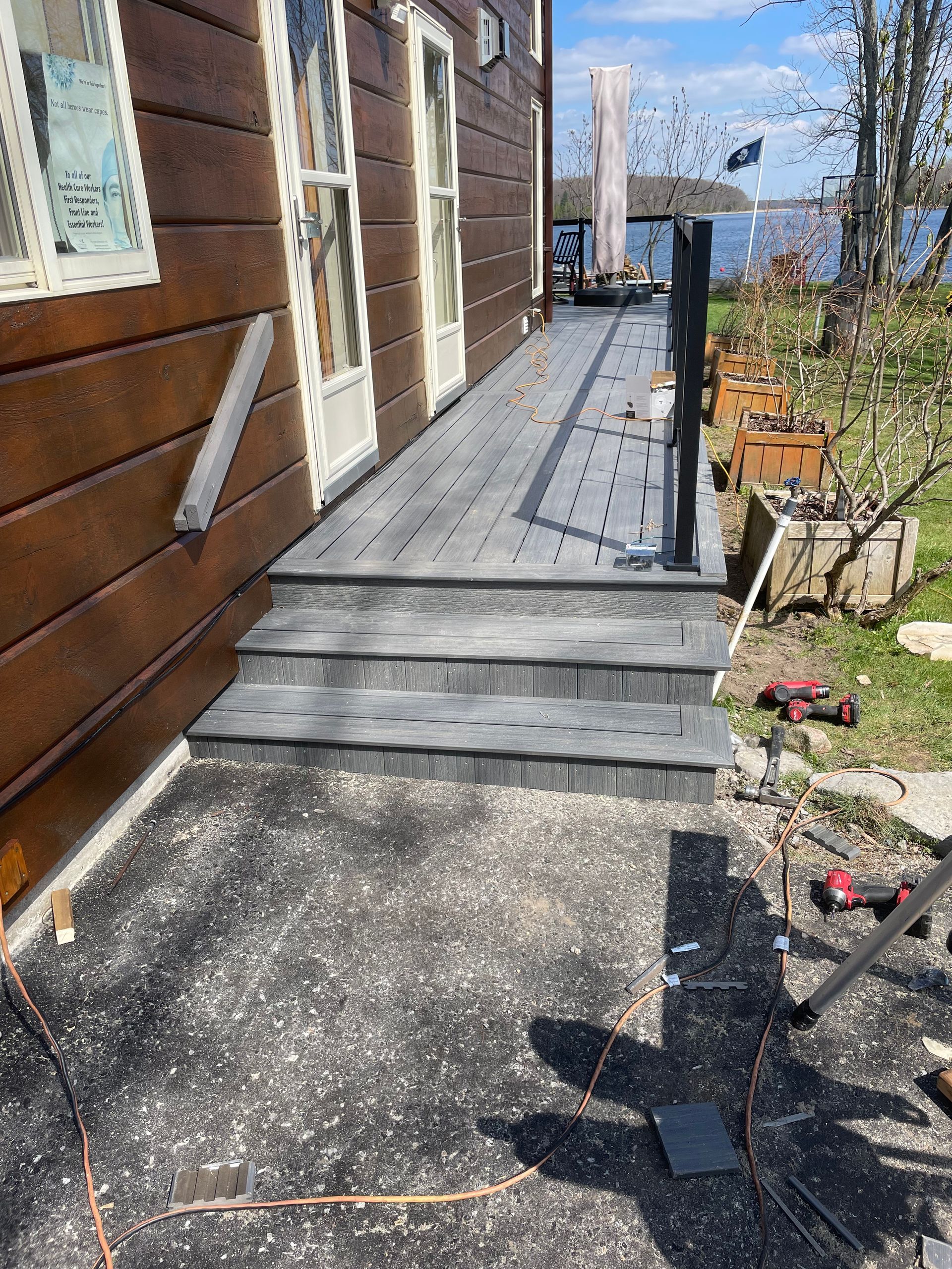 Exterior view of a deck with steps leading to a house, gray composite decking, water in the background.