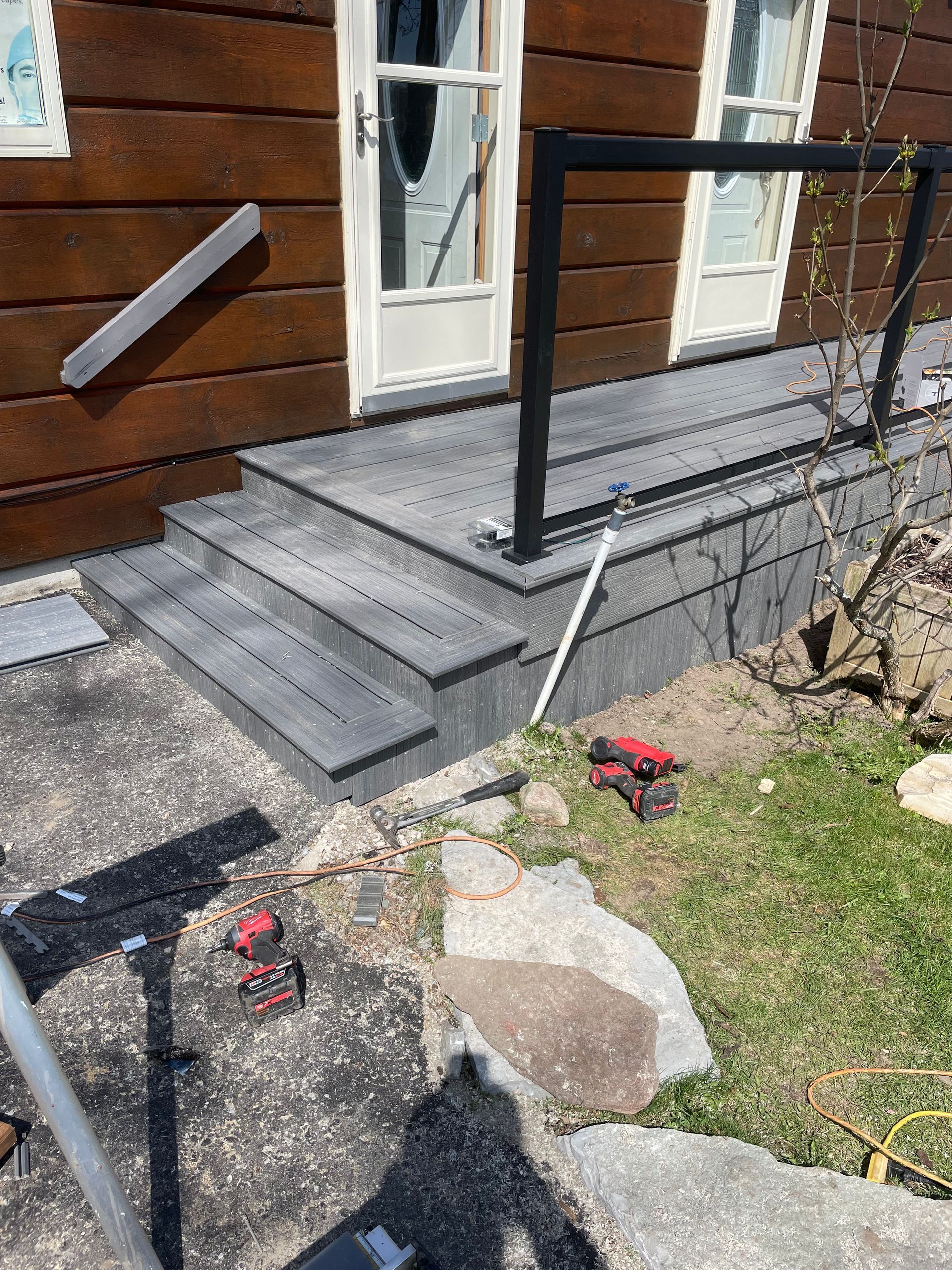 Wooden deck with three steps, black railing, and a wooden building in the background.