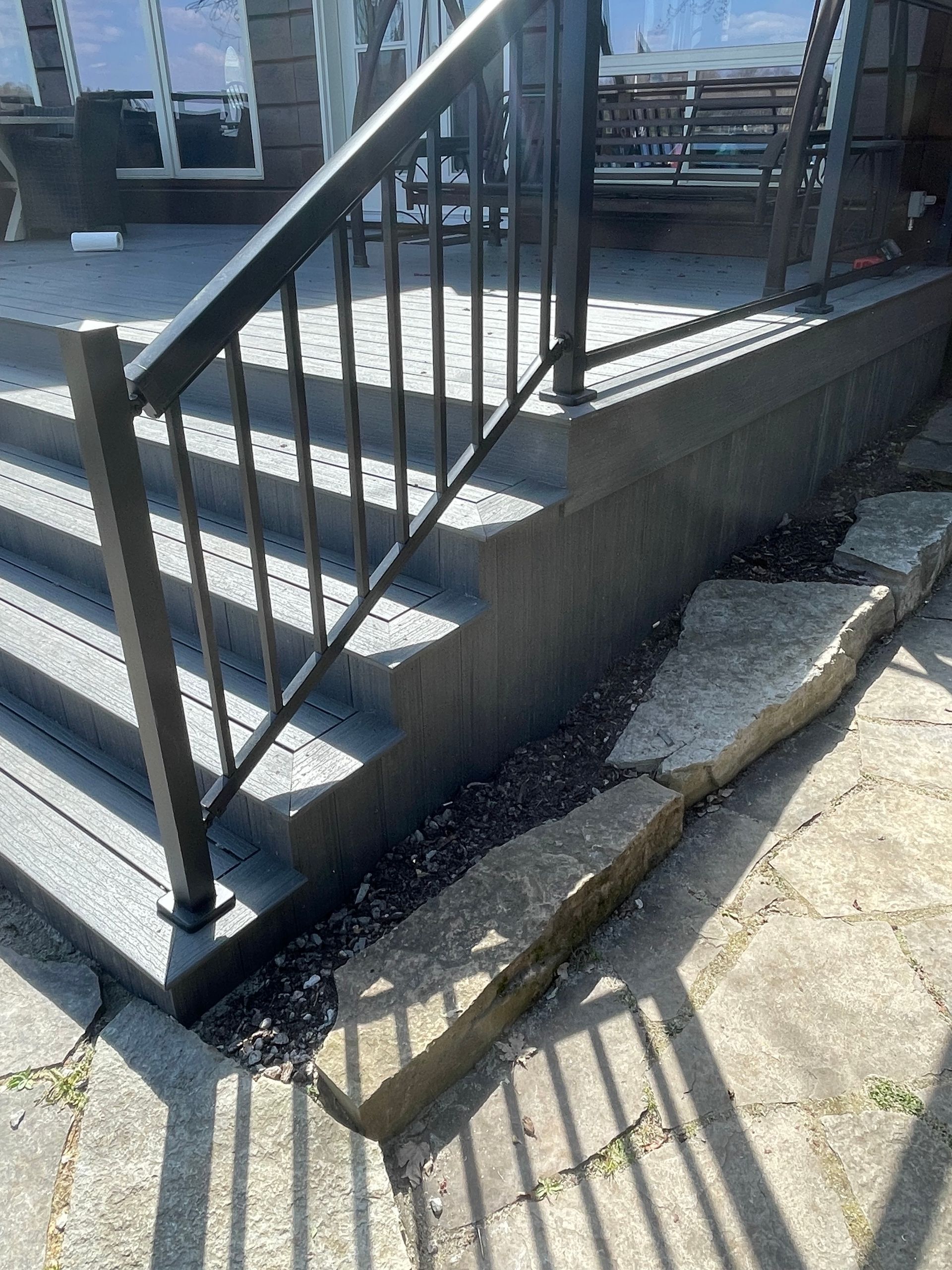 Stairs with black railing leading up to a deck. Concrete wall and stone border visible.