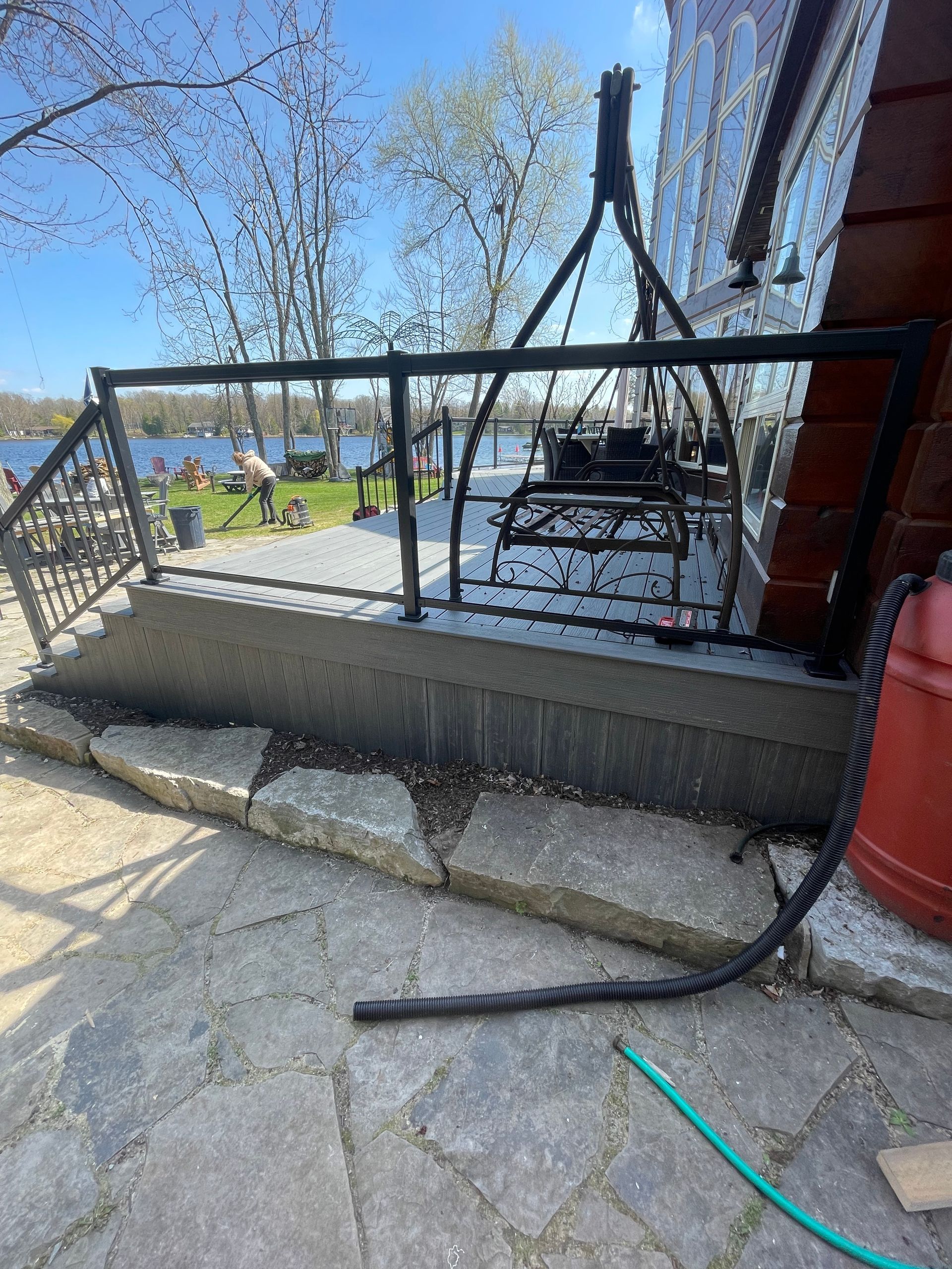 Patio with a black railing, swing, and stone steps, near a lake.