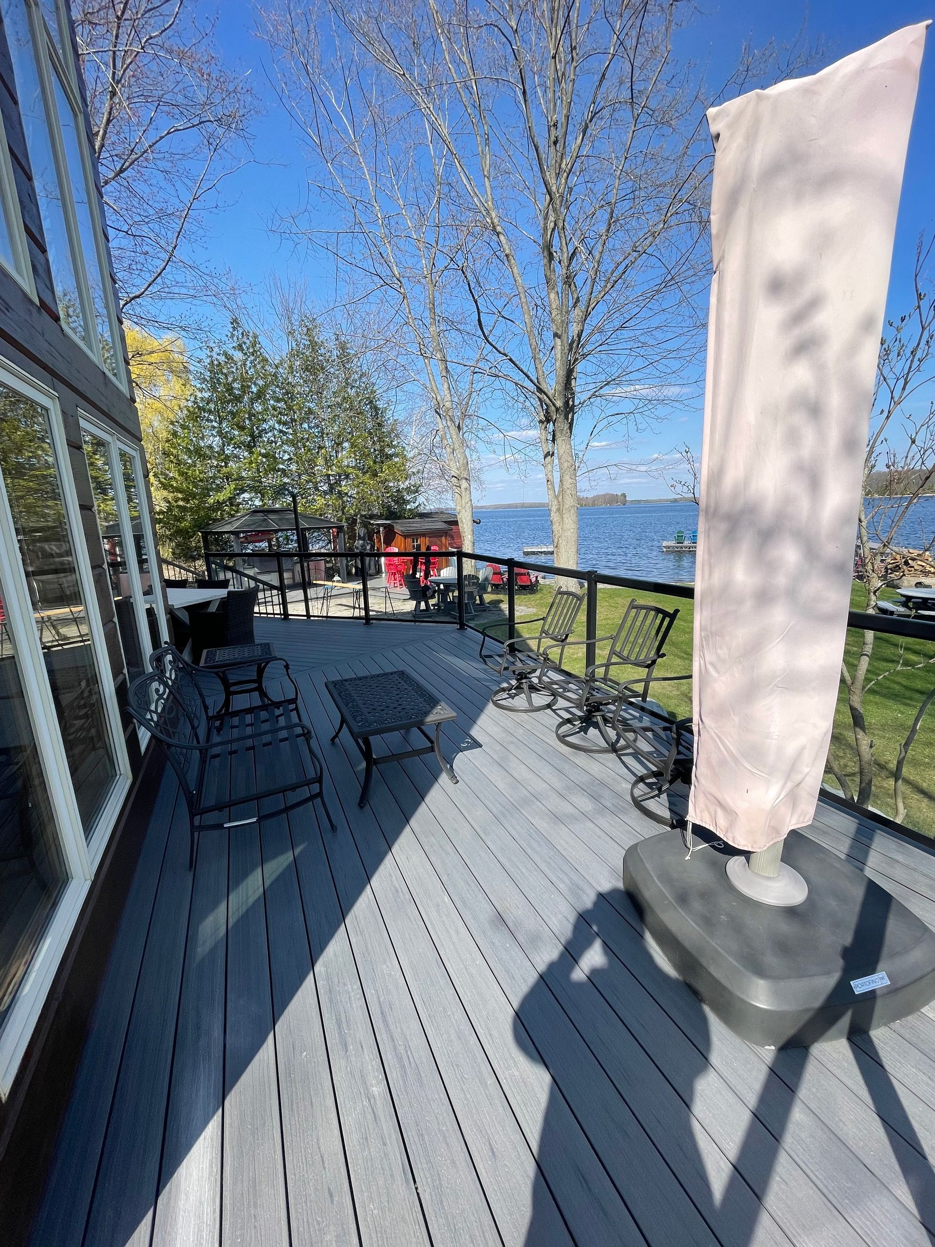 Gray deck overlooking a lake with patio furniture, a covered umbrella, and a house.