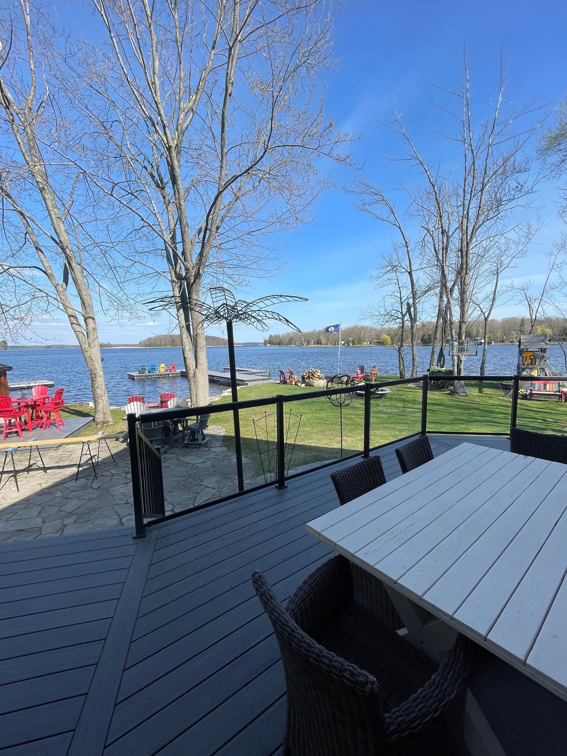 Deck overlooking a lake with a table and chairs, trees and a blue sky in the background.