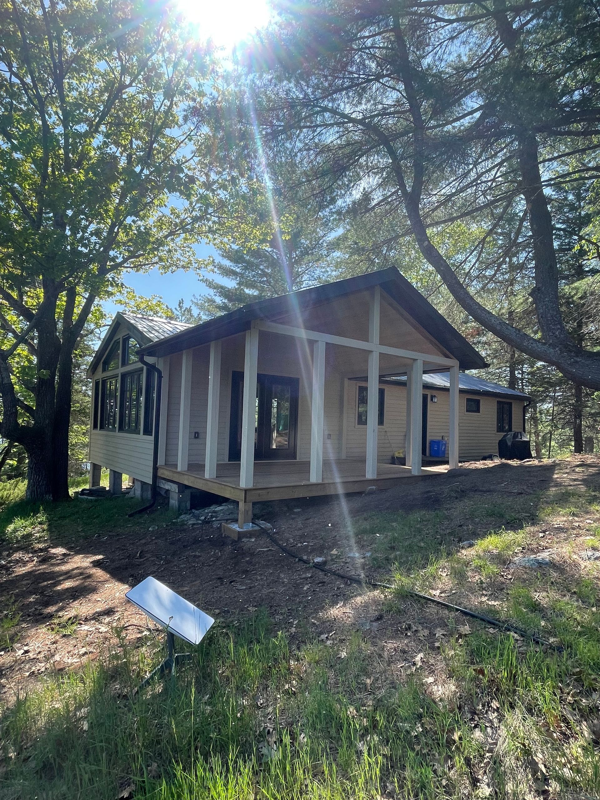 Cabin with porch surrounded by trees on a sunny day.