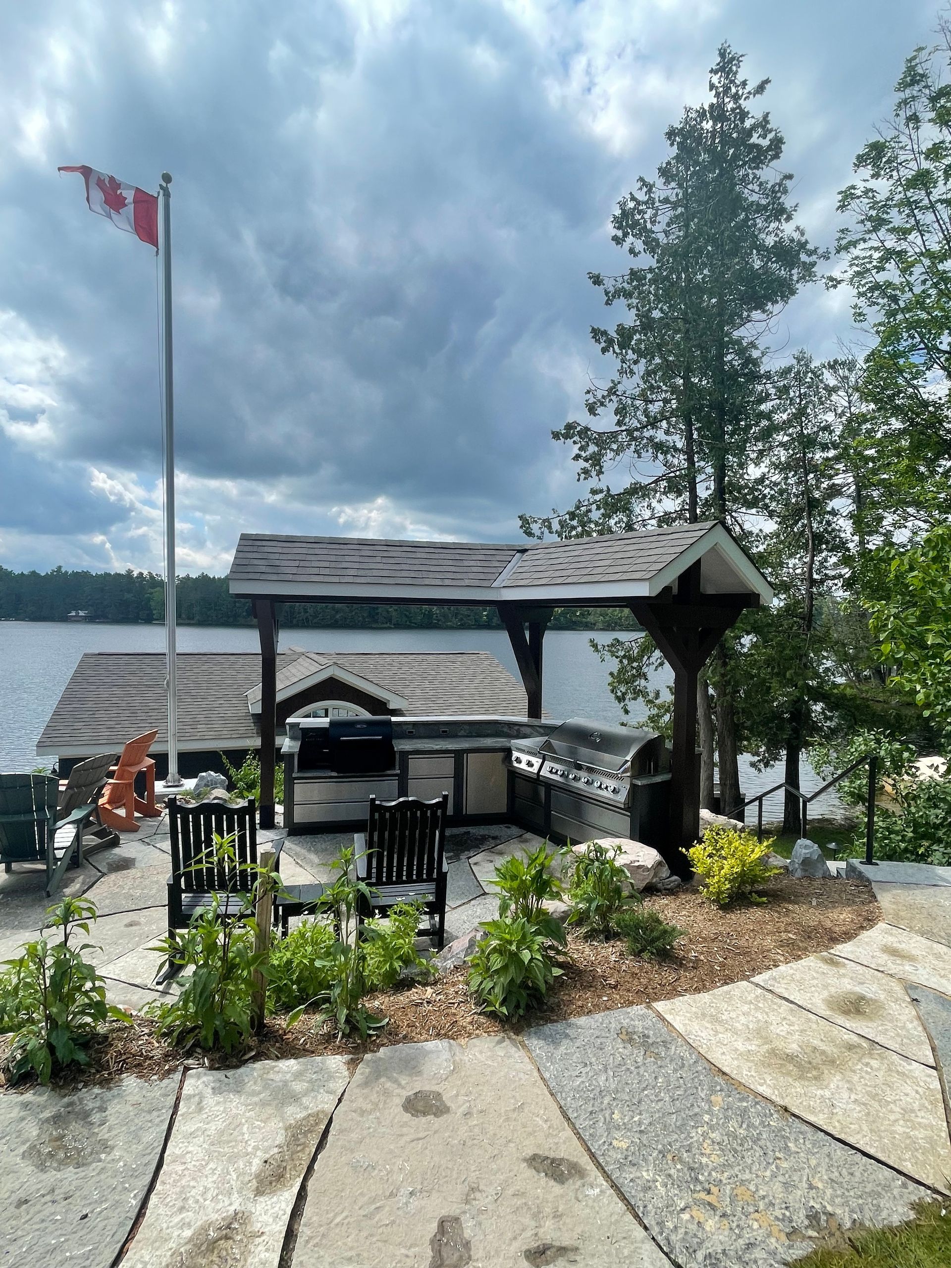 Outdoor kitchen on a lake. A covered grill station with seating and a Canadian flag. Overcast sky.