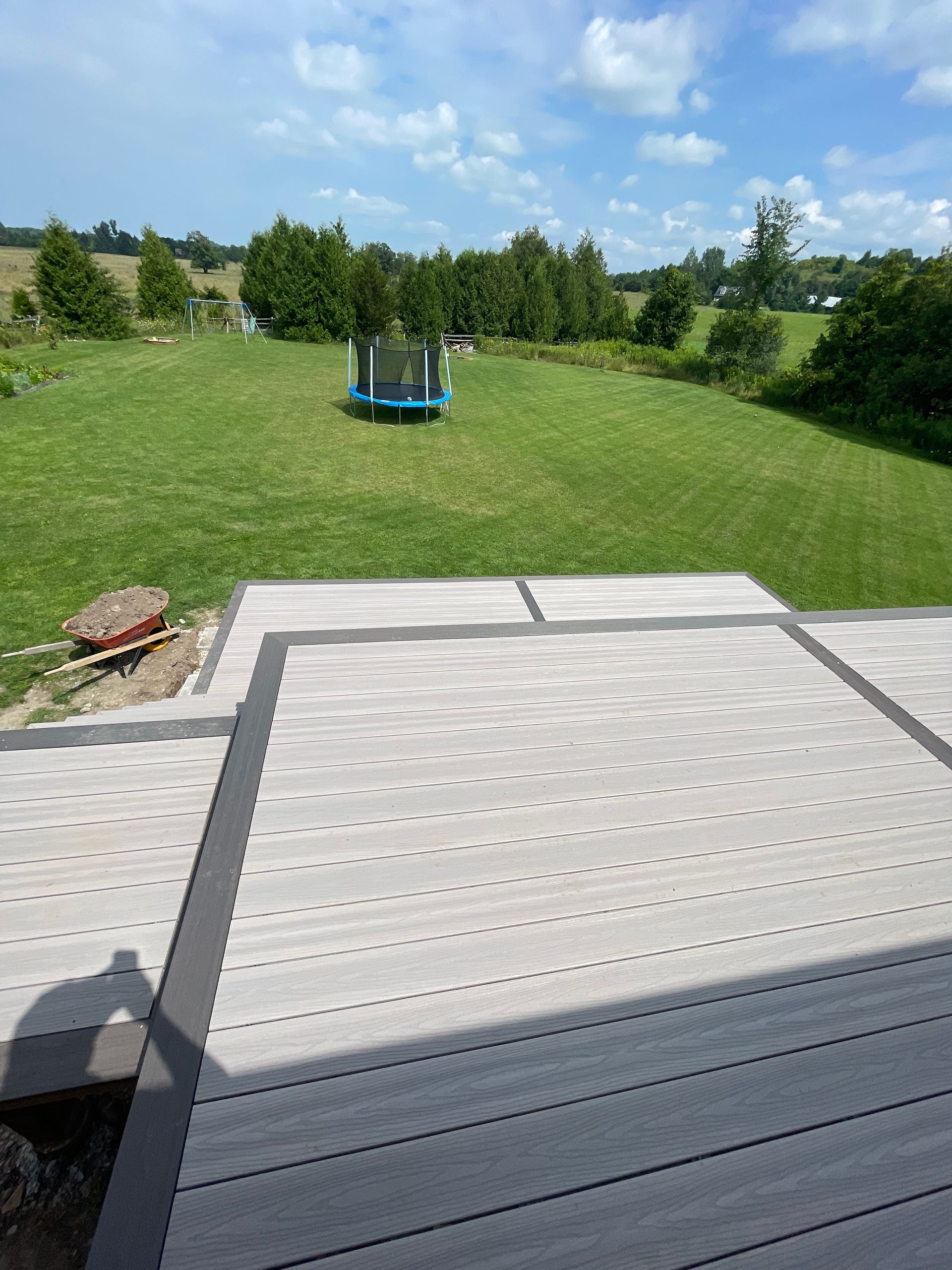 Composite deck overlooking a grassy backyard with a trampoline under a blue sky.