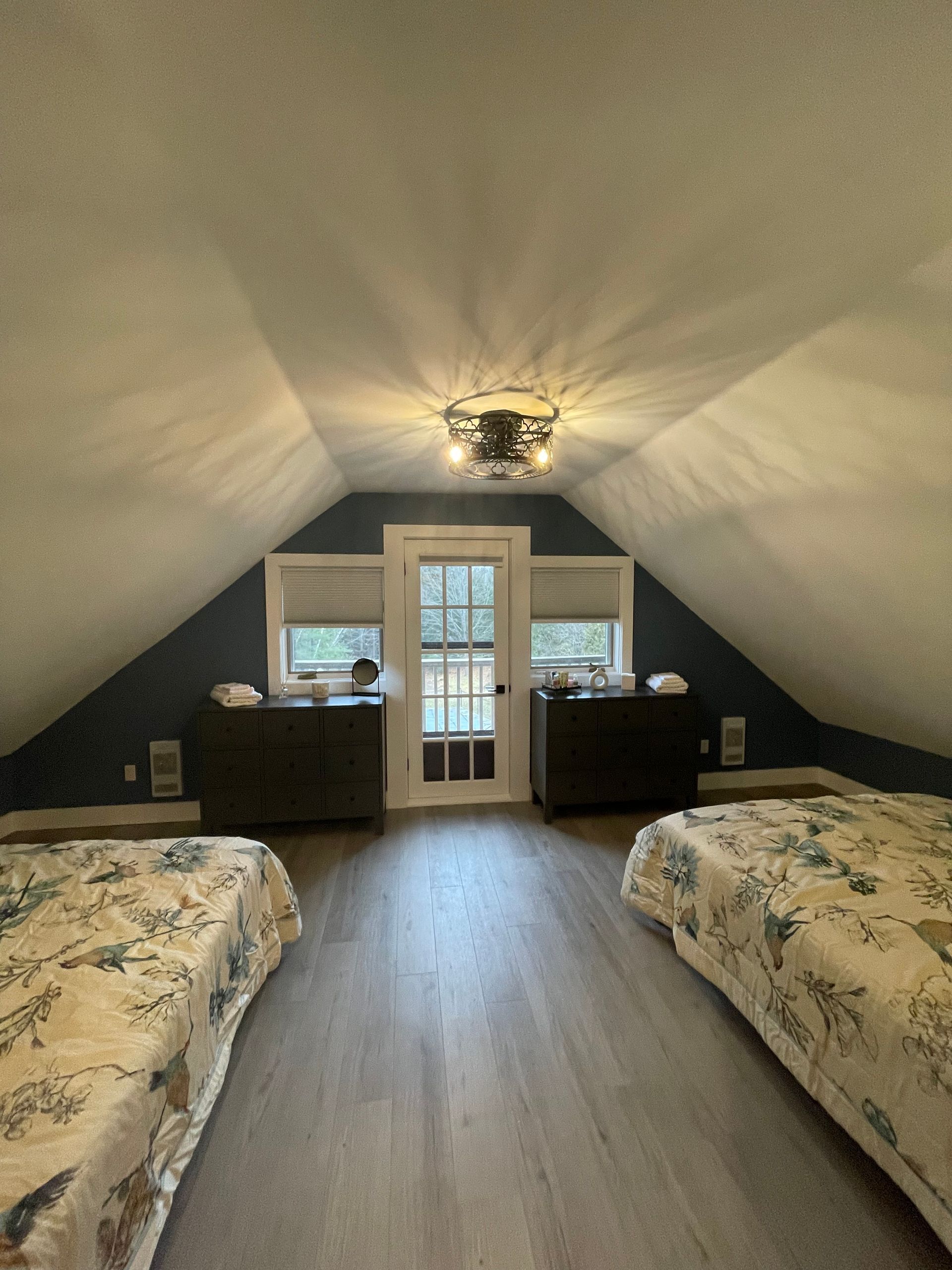 Attic bedroom with two beds, dark walls, door to outdoors, and a ceiling fan.
