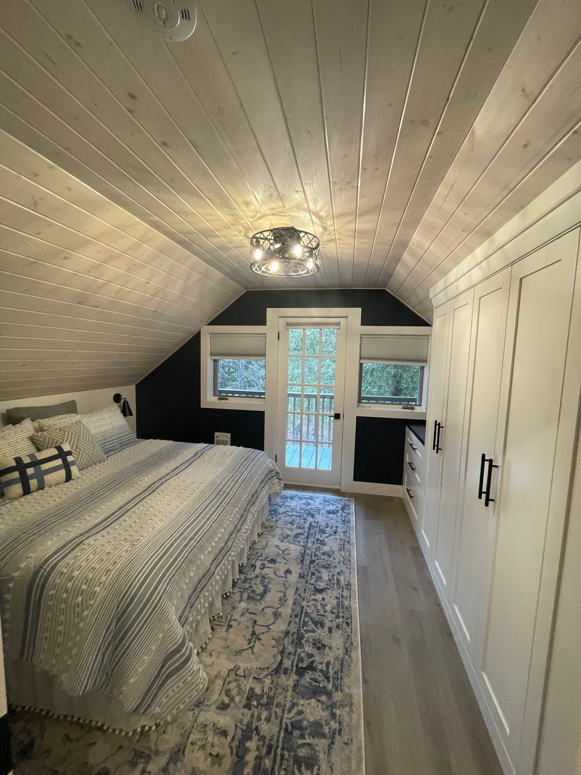 Bedroom with sloped ceiling, door to balcony, built-in closet, and bed with patterned bedding.
