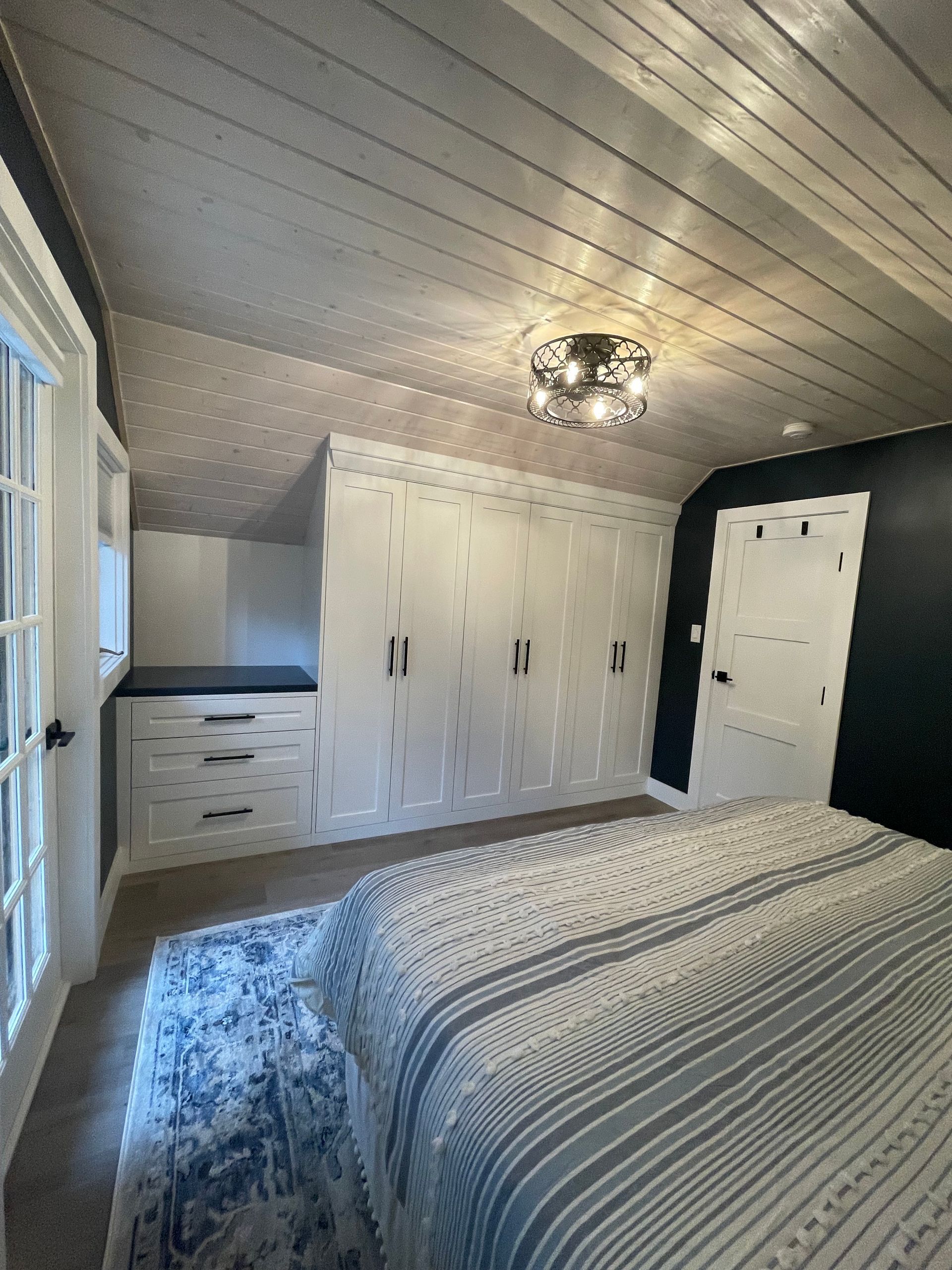 Bedroom with built-in white cabinets, a bed with blue striped bedding, and a decorative ceiling light.