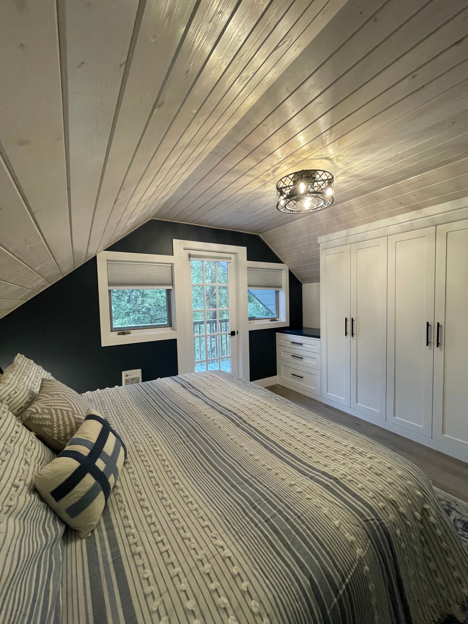 Bedroom with slanted ceiling, white and blue bedding, white closet, and a door to outdoors.