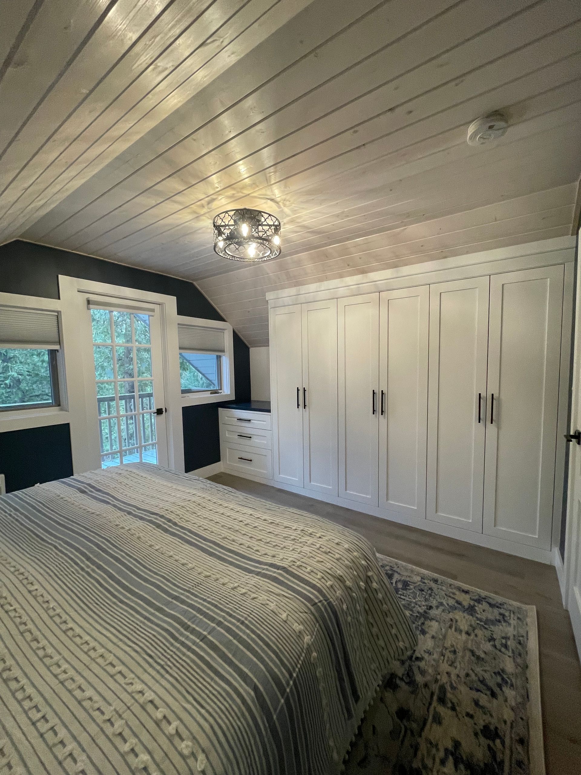 Bedroom with white built-in cabinets, a bed with a striped quilt, and a doorway leading outside.