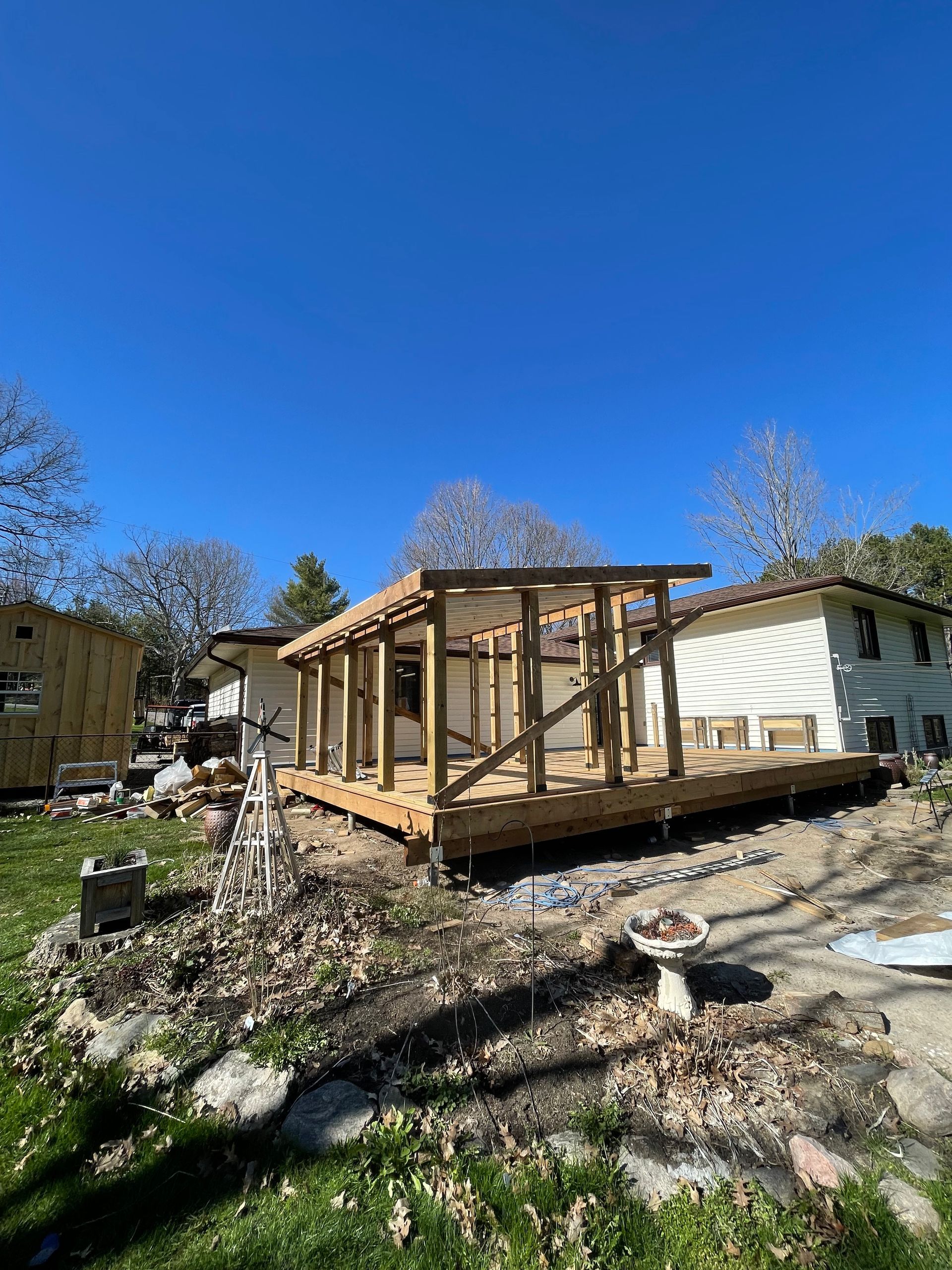 Wooden deck under construction next to a house with blue sky and scattered debris.