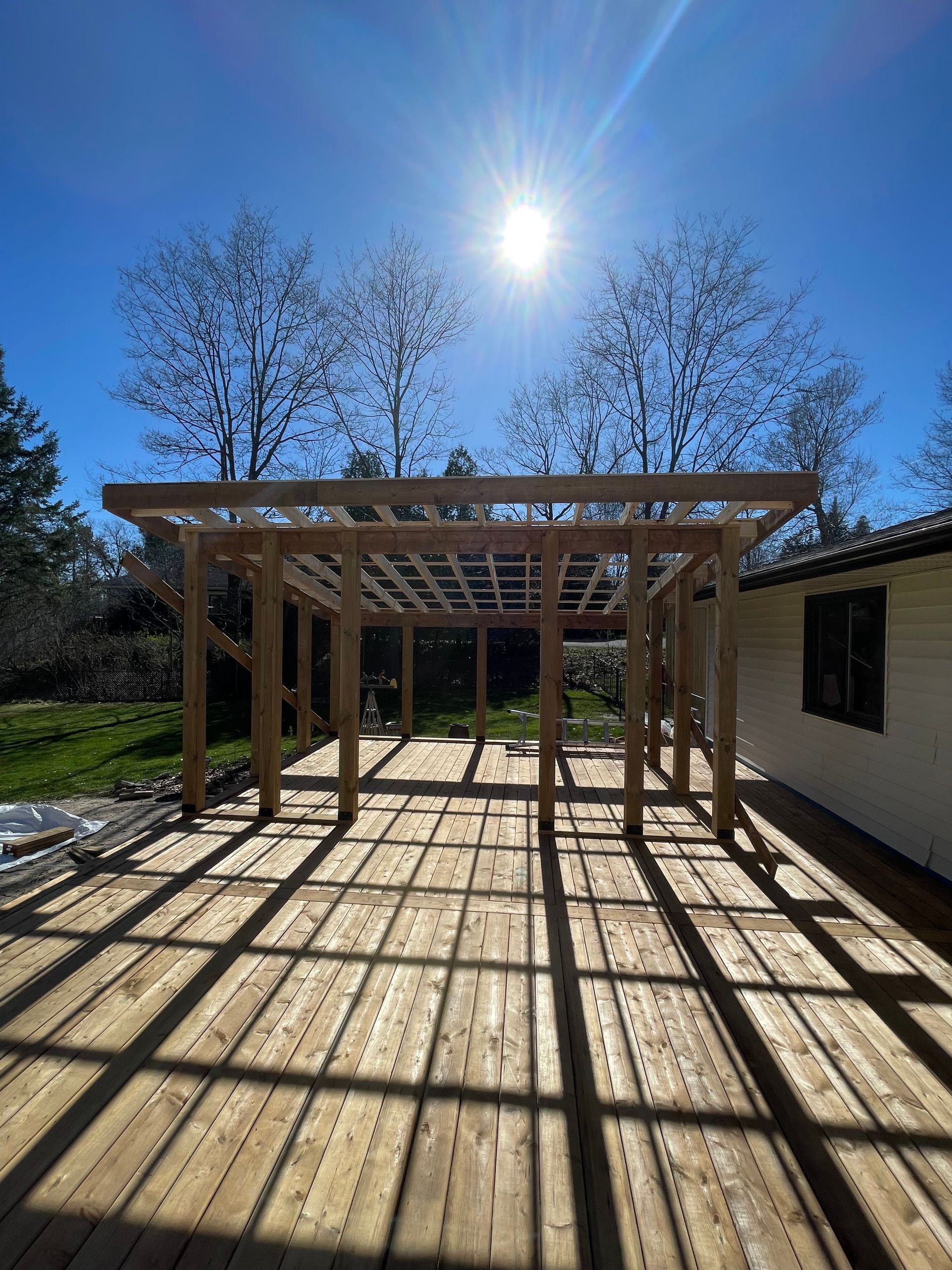Wooden pergola with grid roof casting shadows on a wooden deck in sunny outdoor setting.