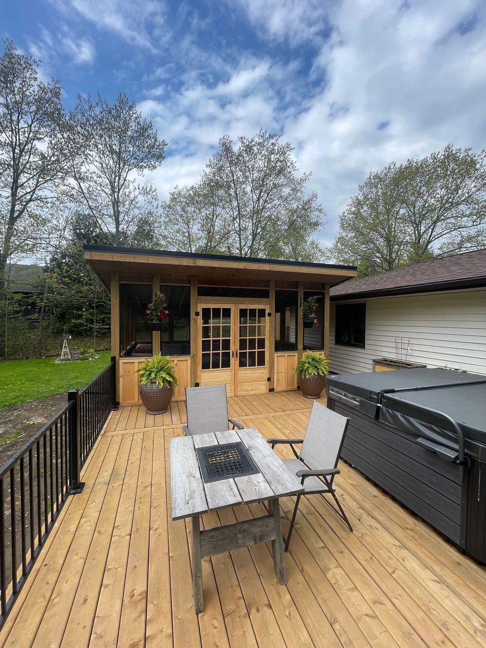 Wooden deck with patio table and chairs facing a small cabin under a cloudy sky