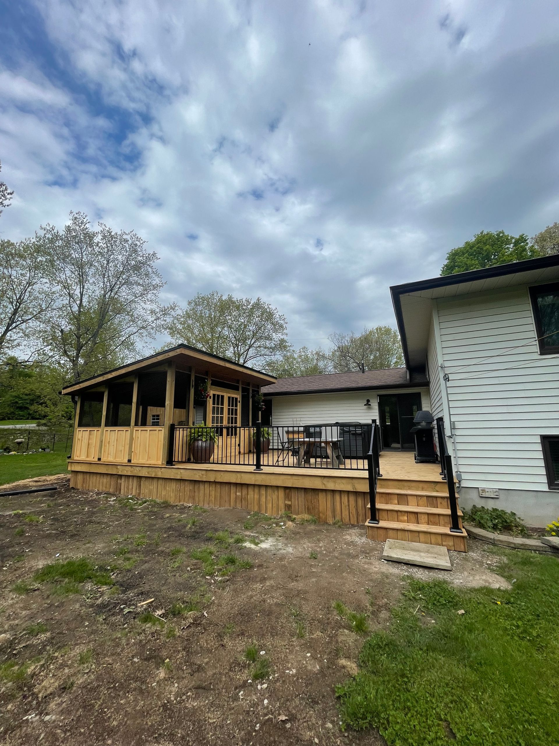 Wooden deck with covered gazebo and steps next to a house with white siding under a cloudy sky.