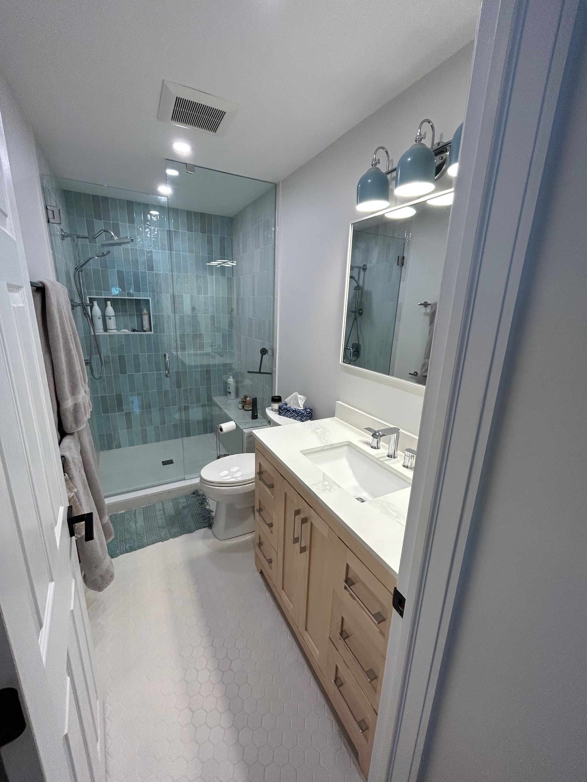 Bathroom with blue tile shower, beige vanity, white toilet and sink, grey walls.