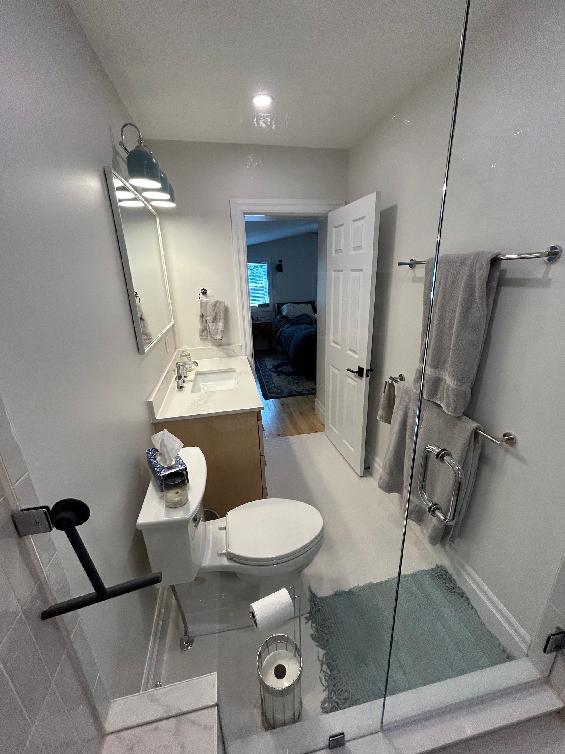 Bathroom with a toilet, sink, and shower. A door leads to a bedroom.
