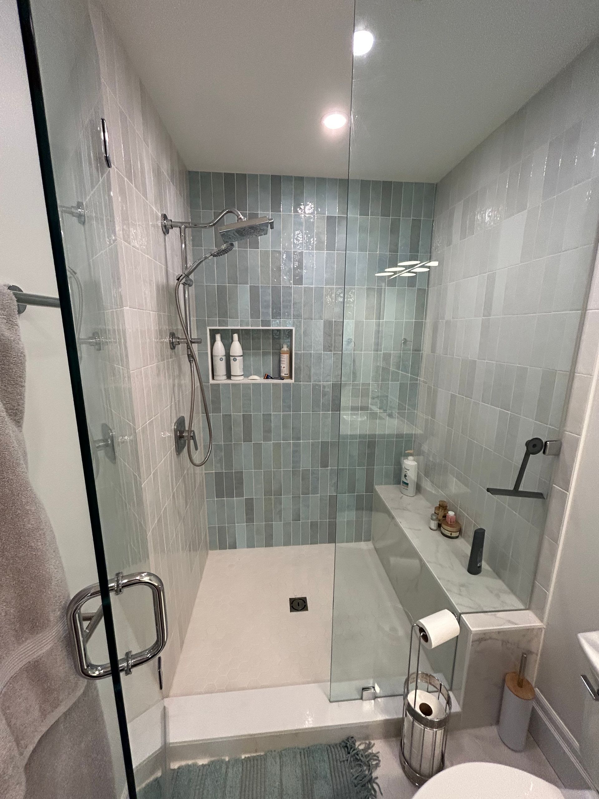 Modern bathroom with glass shower, blue tile walls, and a white bench.