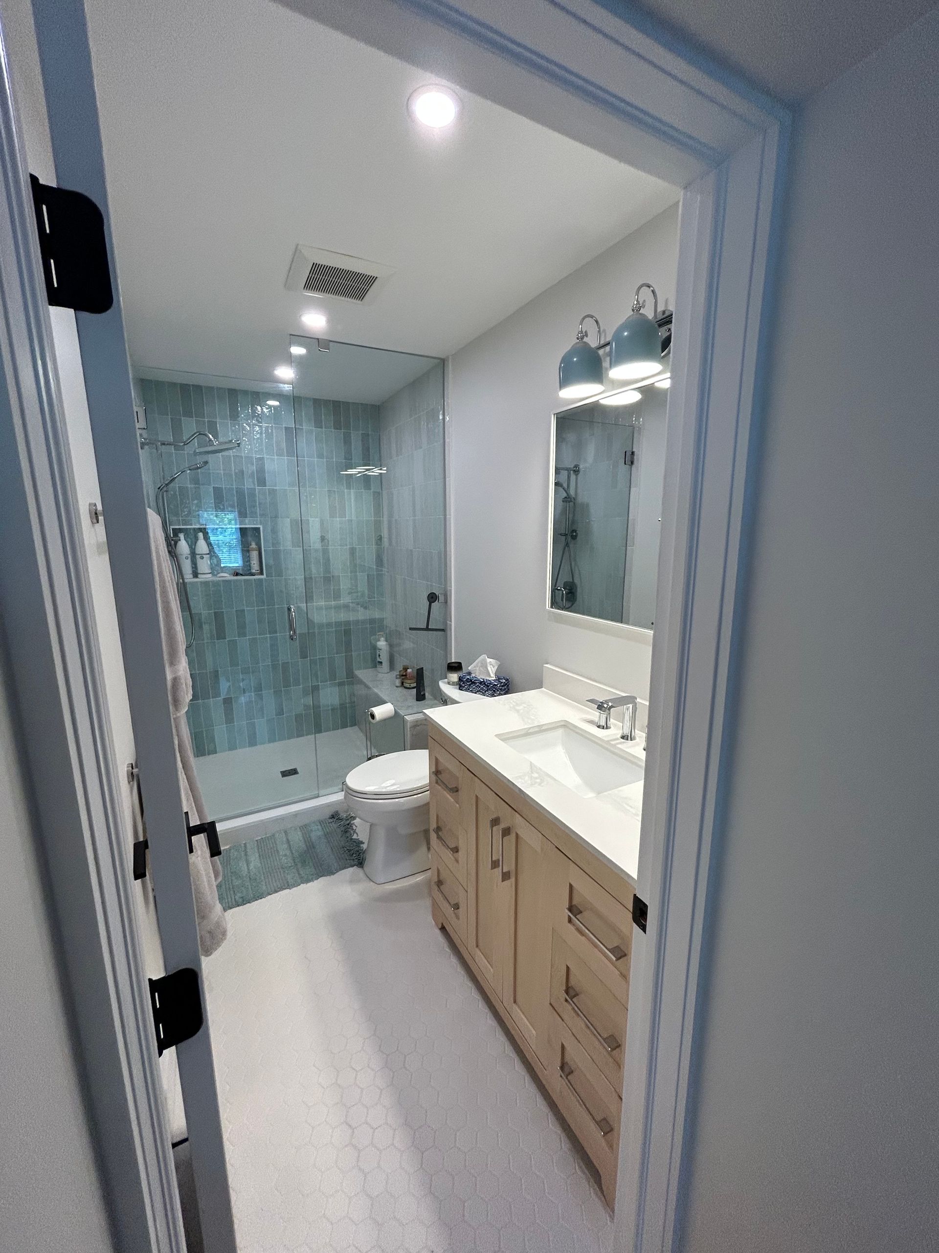 Bathroom with a shower, toilet, vanity, and a light color scheme. Door frame in view.