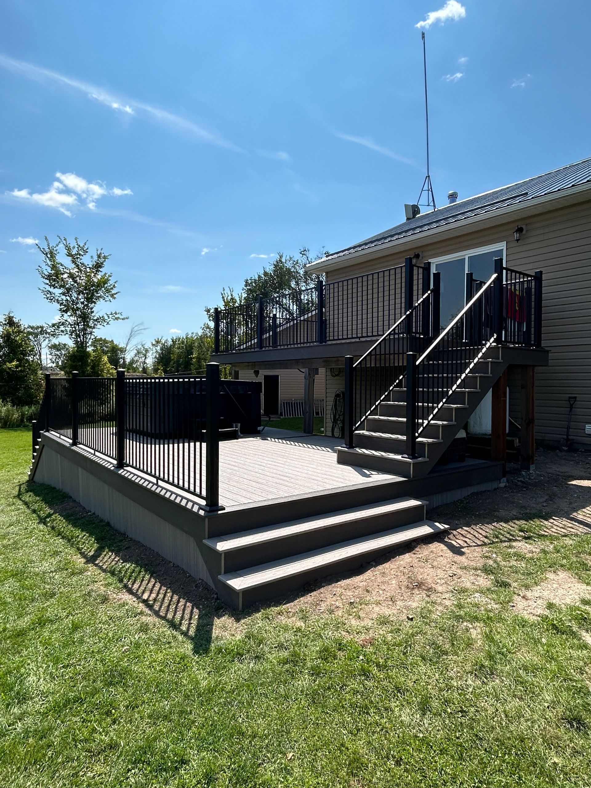 A two-tiered deck with black railing and stairs leading to a house, on a sunny day.