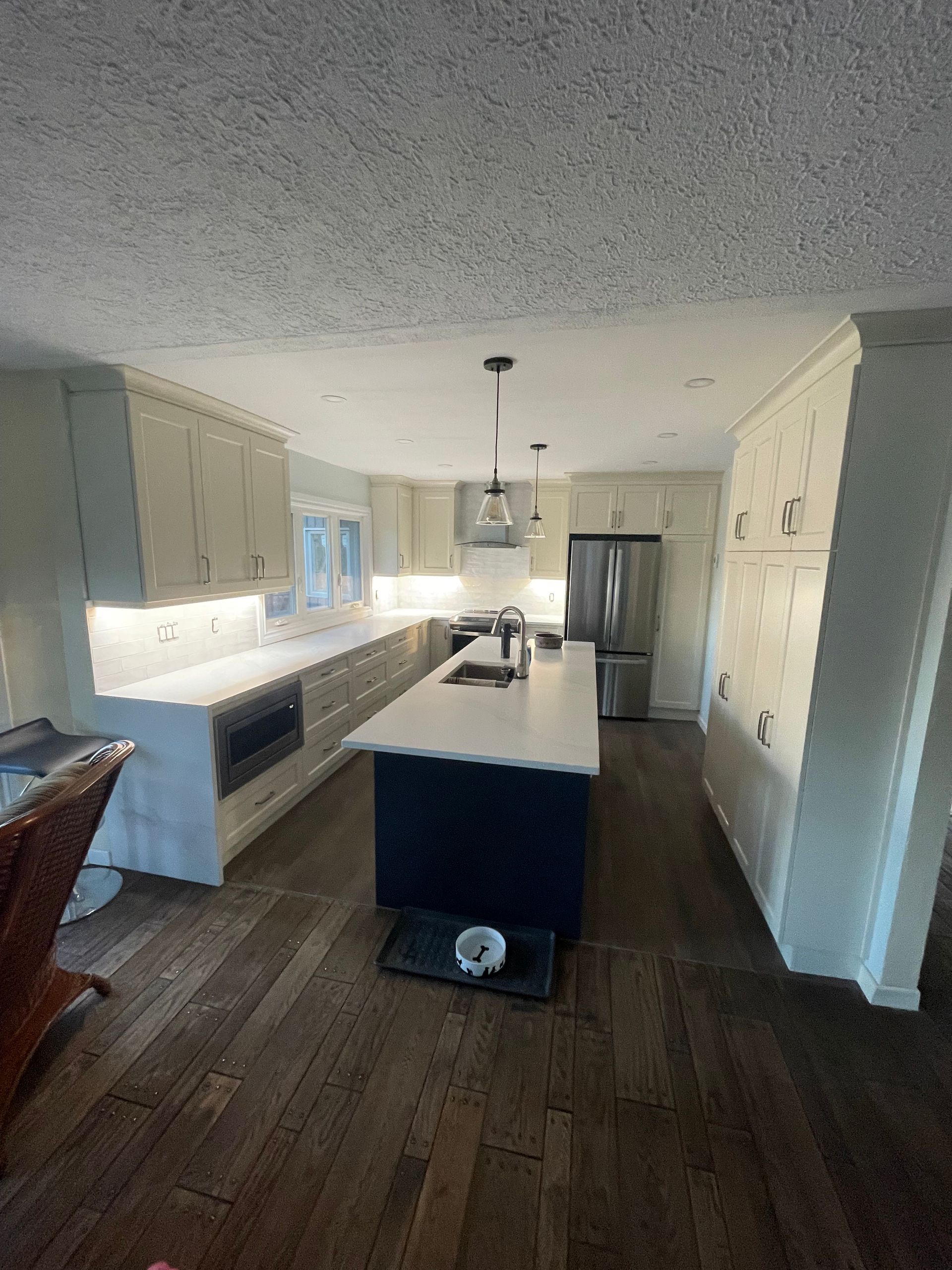 Modern kitchen with white cabinets, dark wood floors, and a large island under pendant lights.