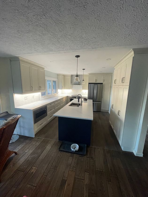 Modern kitchen with white cabinets, dark wood floors, central island, and stainless steel refrigerator