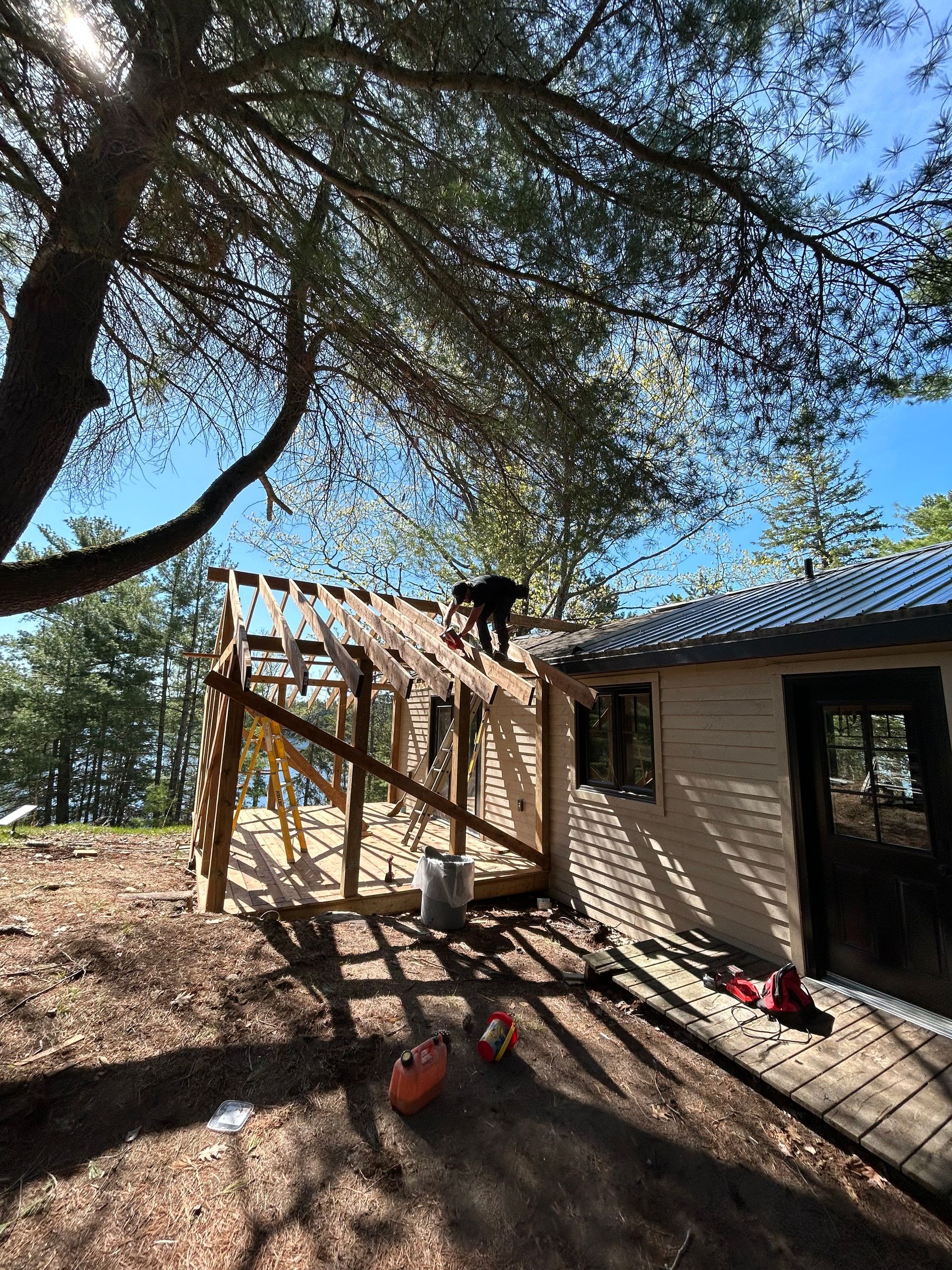 Outdoor construction site beside a house, with wooden stairs under a large tree and bright sunlight.