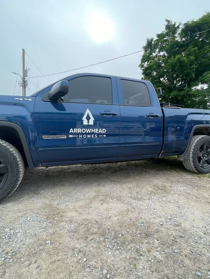 Blue pickup truck with company logo parked on gravel under a cloudy sky.