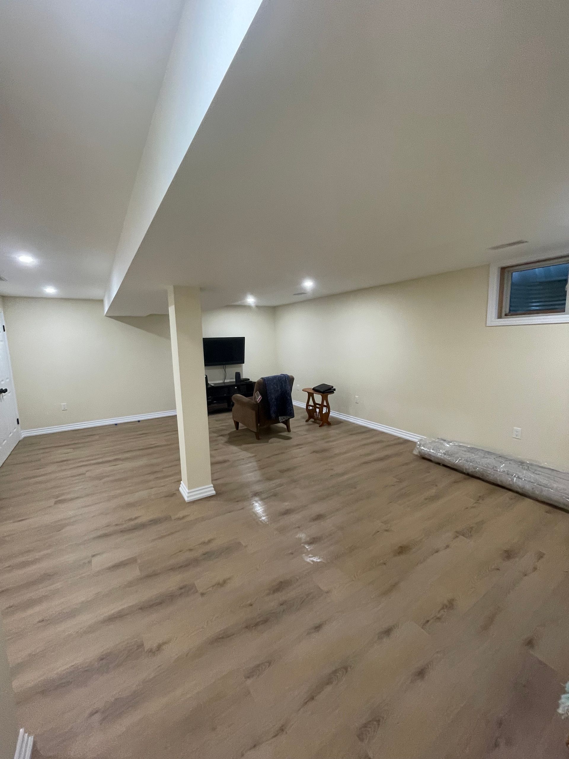 Empty basement with wood flooring, recessed lights, a support column, and a small desk in the back corner
