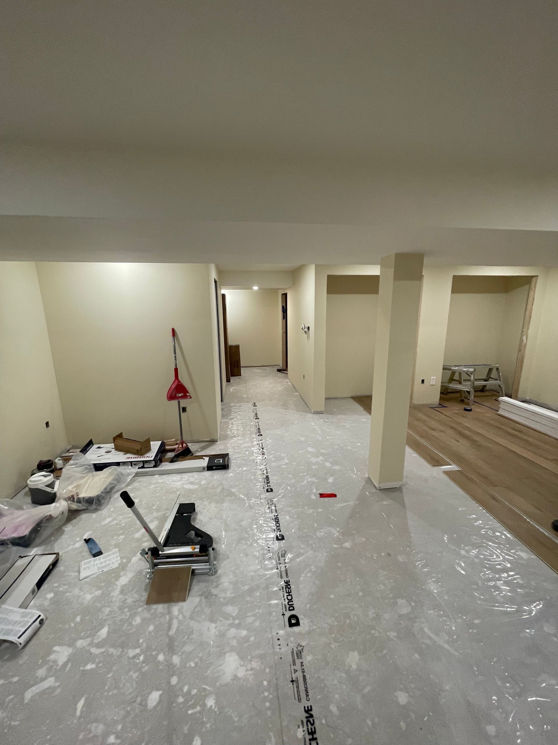 Renovation site with plastic-covered floor, tools, paint buckets, and unfinished walls and columns
