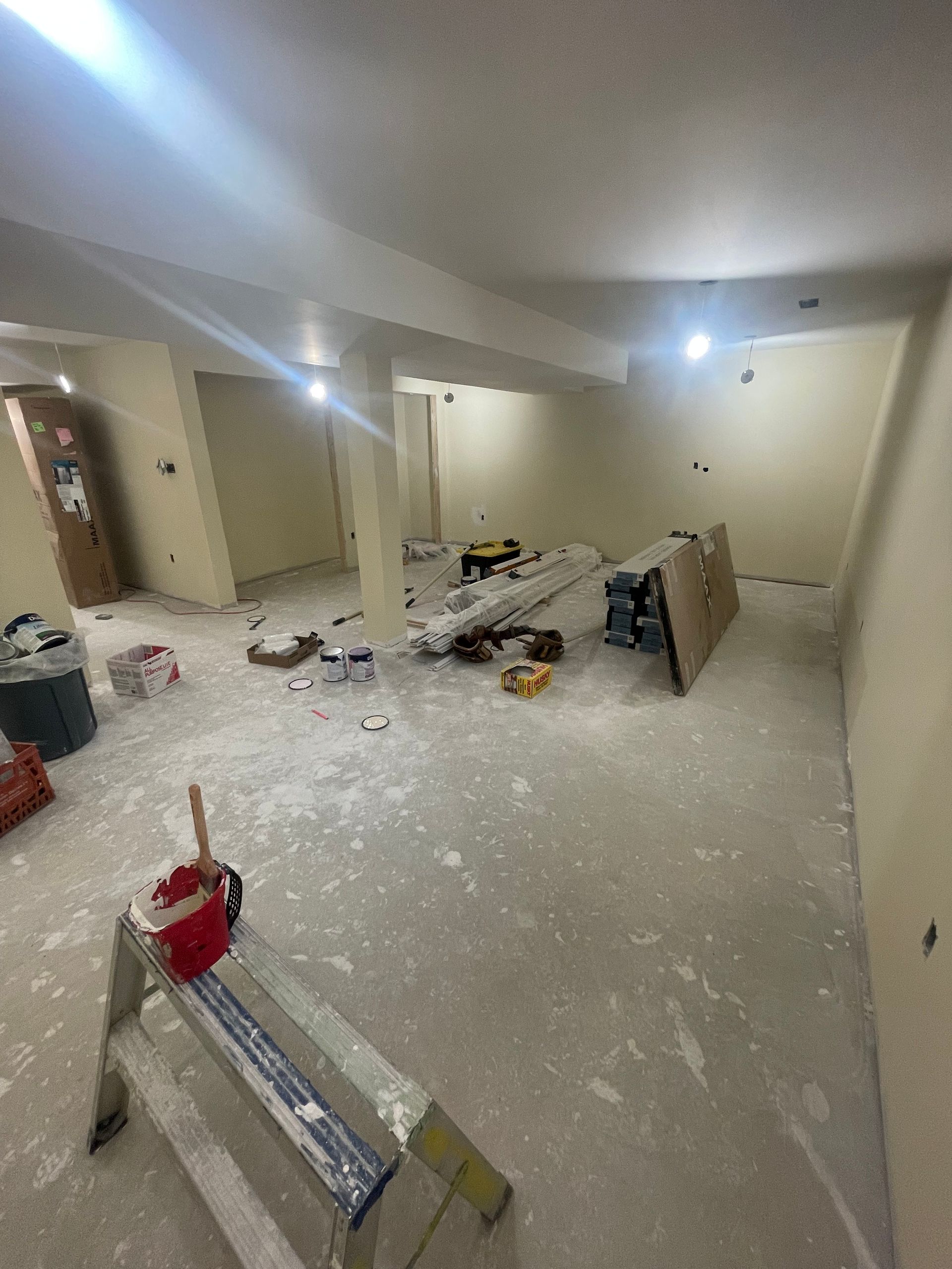 Unfinished basement room with drywall dust, tools, and construction materials scattered on the floor.