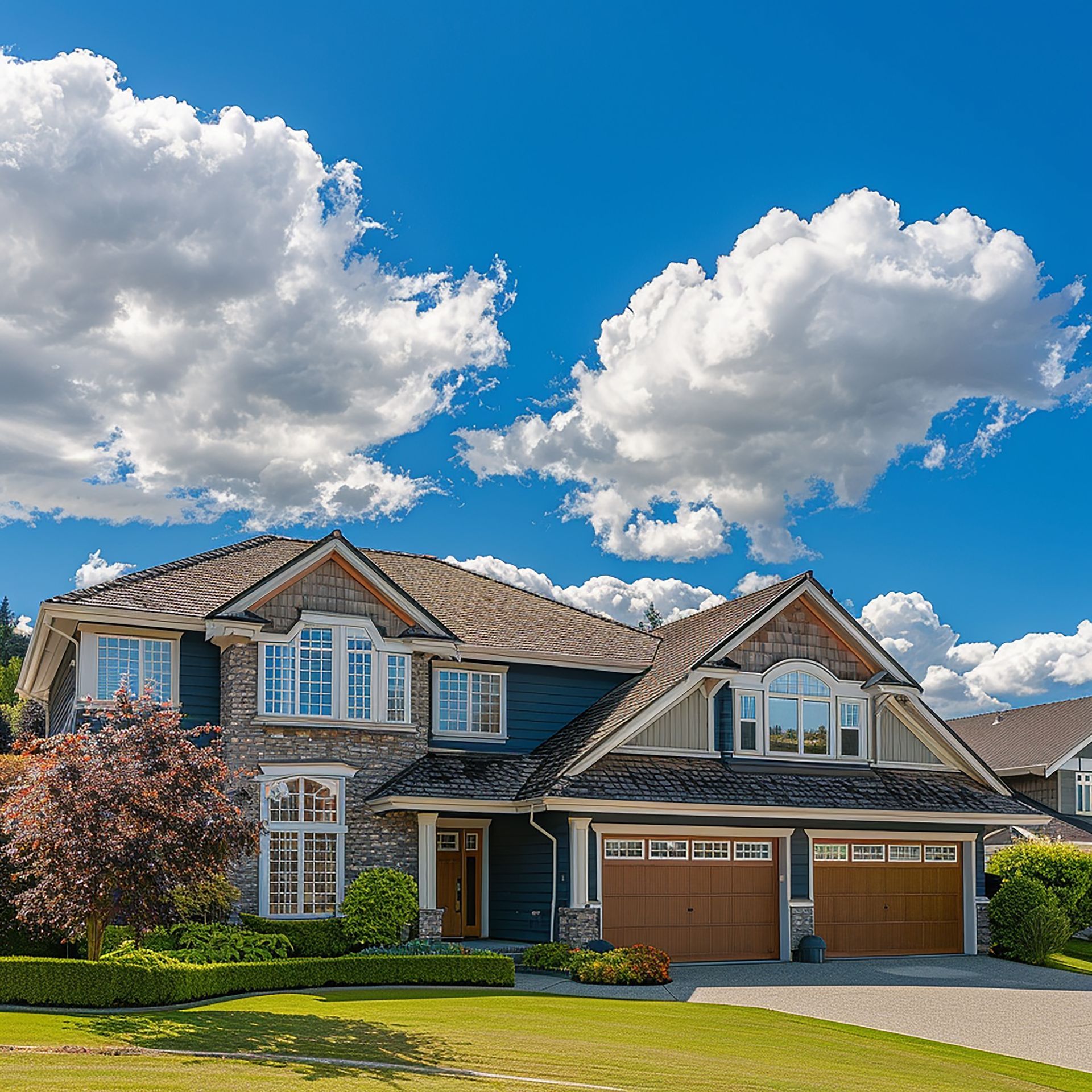 Large house with blue siding, stone accents, and two-car garage under a bright blue sky with puffy clouds.