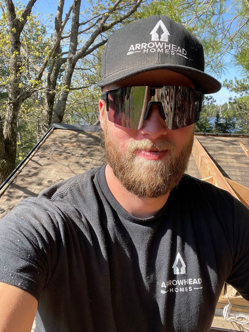 Man wearing a black cap, mirrored sunglasses, and black shirt outdoors in bright sunlight.