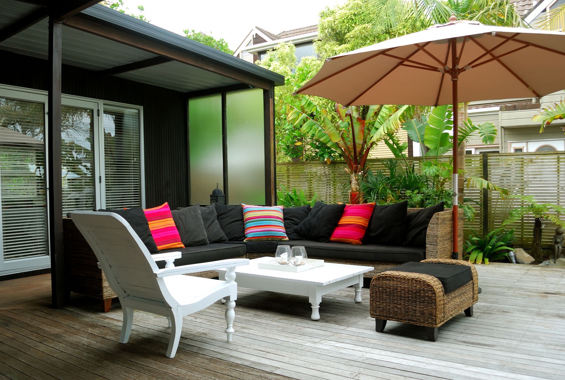 Outdoor lounge area with black sectional, white chair, coffee table, and umbrella.