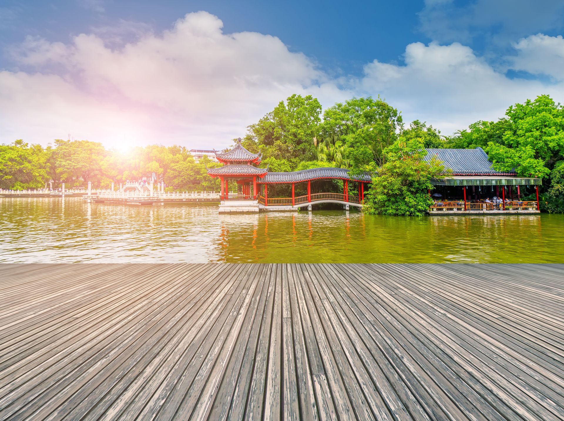 Wooden dock overlooking a lake with traditional Chinese pavilions and lush green trees under a blue sky.