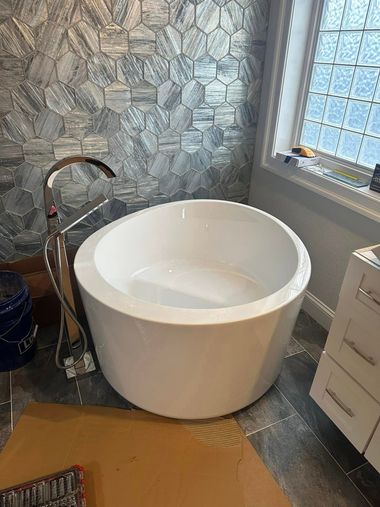 Modern bathroom with a white freestanding tub, stone tile wall, and window blinds