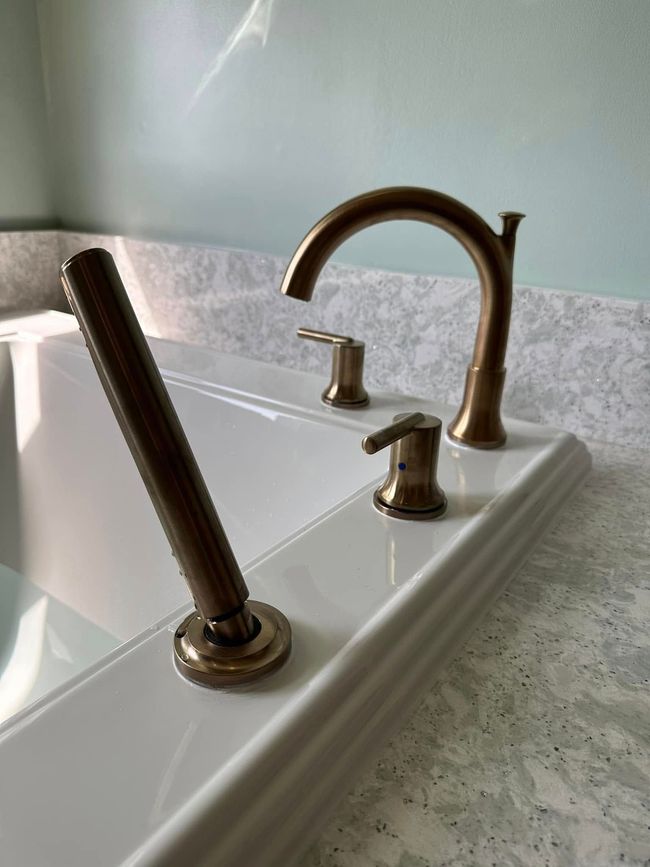 Bathroom sink with bronze faucet and a tilted soap dispenser on a white countertop.