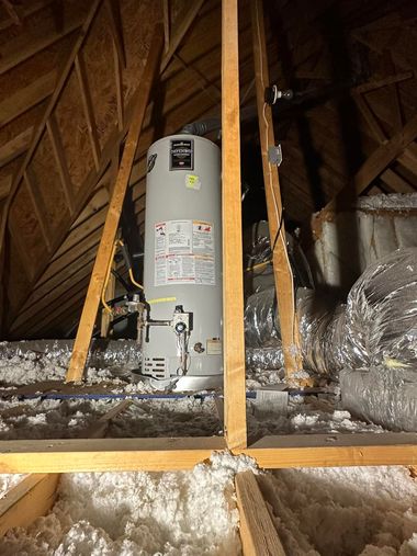 Water heater in an attic with exposed insulation and wooden rafters.