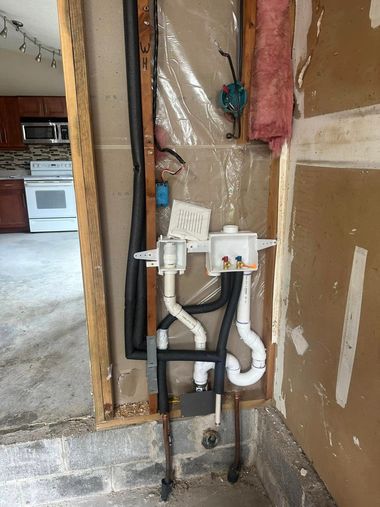 Exposed plumbing and pipes in an unfinished wall beside a kitchen area