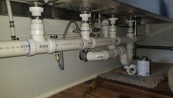 Undersink plumbing with PVC drain pipes, valves, and fittings beneath a cabinet