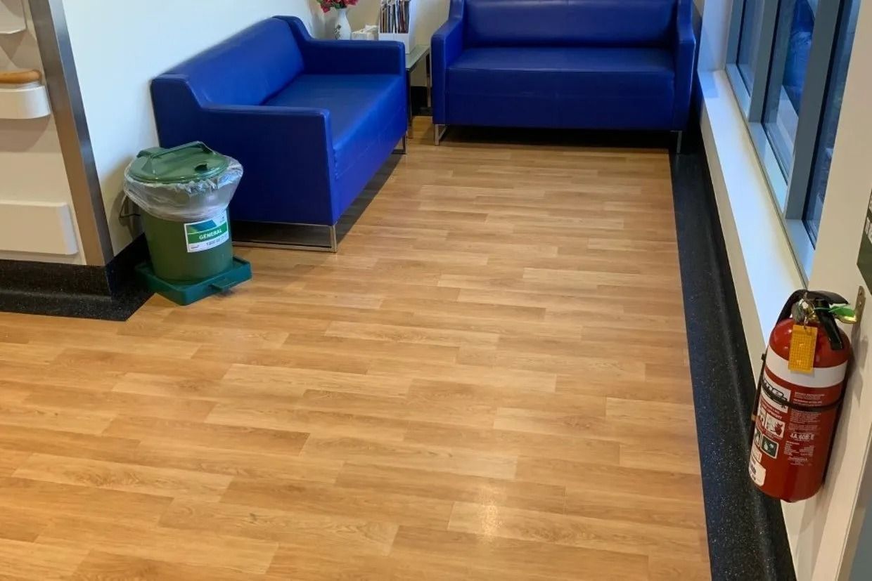 Waiting area with blue couches, wood-look flooring, trash can, and fire extinguisher. — Ozwide Flooring In Ciccone, NT