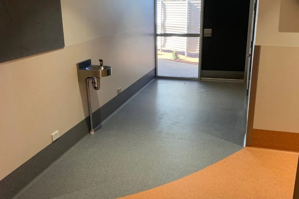 Hallway With Water Fountain on the Left, Open Door at the End. Grey Floor, Tan Walls — Ozwide Flooring In Ciccone, NT