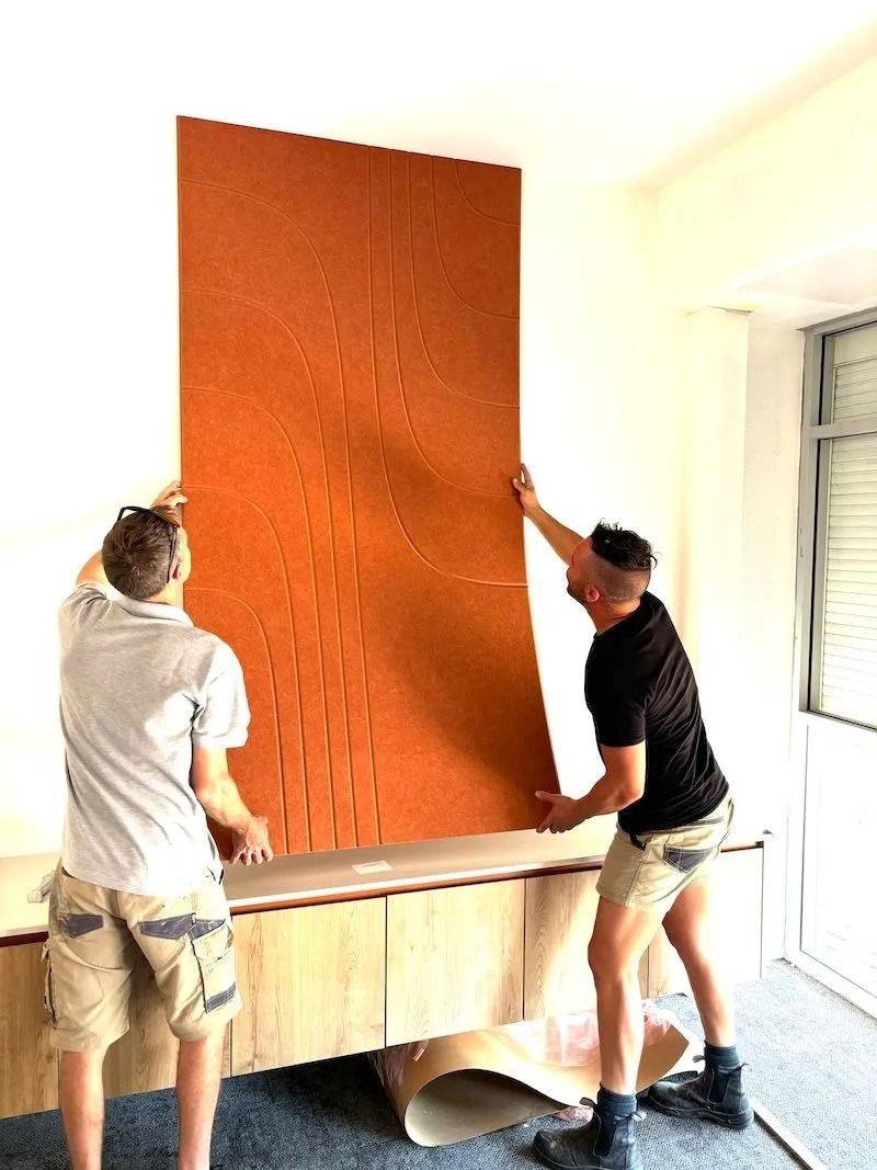 Two People Installing Large Orange Wall Panel Over a Wooden Cabinet — Ozwide Flooring In Ciccone, NT