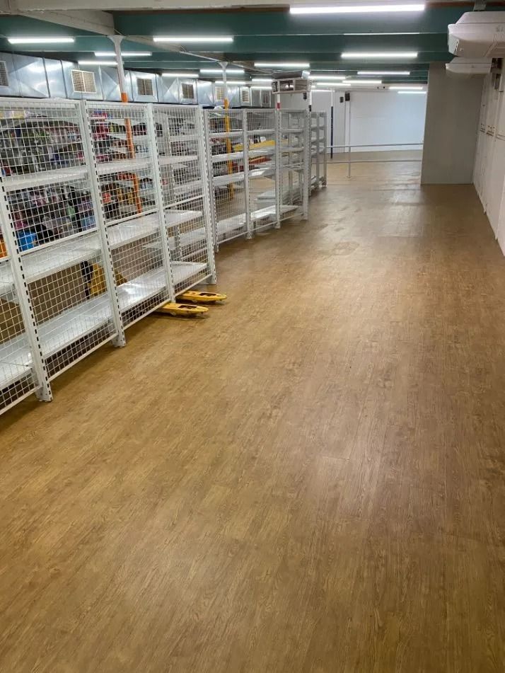A Long Warehouse Aisle With White Shelving Stocked With Goods and a Wooden Floor — Ozwide Flooring In Ciccone, NT