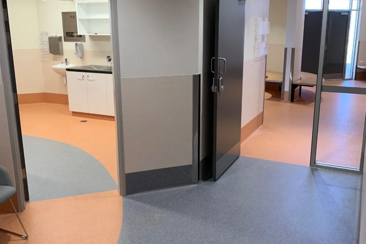 Hallway with open door to a medical room; various flooring colours; a grey door on the right. — Ozwide Flooring In Ciccone, NT