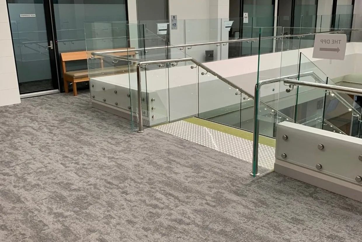 Stairway With Glass Railing, Grey Carpet, and a Wooden Bench — Ozwide Flooring In Ciccone, NT