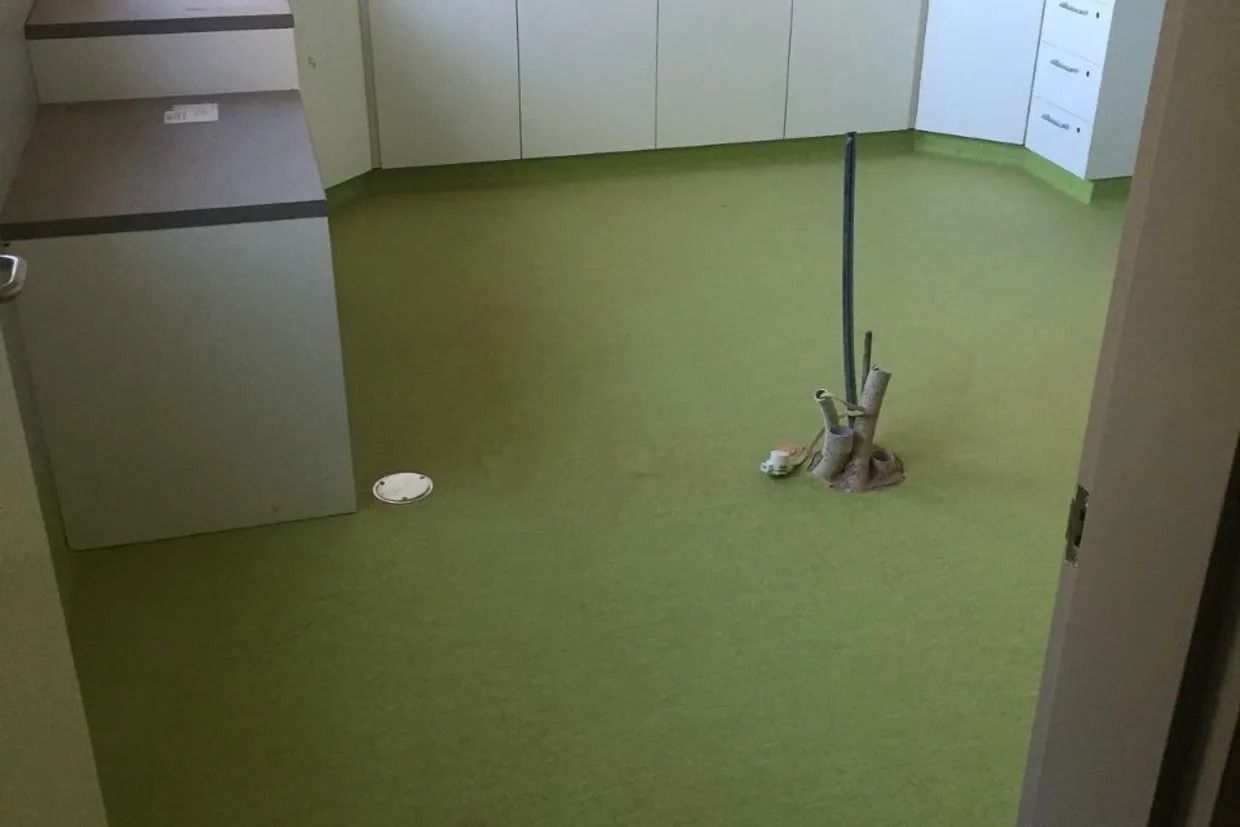 Green Floor in a Room With White Cabinets and a Dark Pipe — Ozwide Flooring In Ciccone, NT