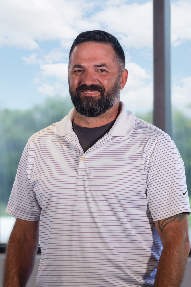 A man with a beard is standing in front of a window wearing a striped shirt.